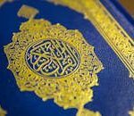 Close-up of intricate gold Quranic calligraphy on a blue cover, showcasing elegant Islamic design.