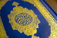 Close-up of intricate gold Quranic calligraphy on a blue cover, showcasing elegant Islamic design.